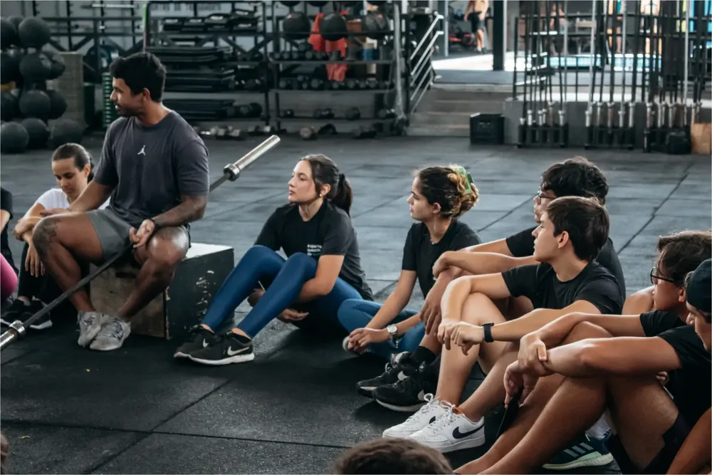 Alunos da AM sentados no chão de uma academia durante um evento presencial